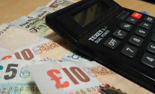 Ilustrasi kalkulator dan uang untuk menghitung total biaya pinjaman online