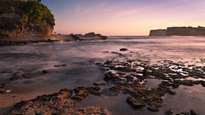 Pesisir berbatu Pantai Pacitan dengan langit senja dan ombak tenang