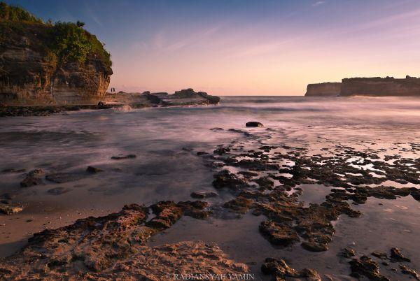 Pesisir berbatu Pantai Pacitan dengan langit senja dan ombak tenang